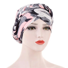 A mannequin wears a pink, grey, and black camouflage print turban with a braided headband detail.