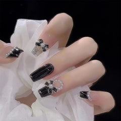 A set of mid-length black coffin-shaped press-on nails decorated with bows and pearl accents.