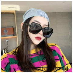 A woman wears oversized square black polarized sunglasses with a grey beanie and a colorful sweater.
