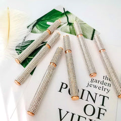 Several glittery, rhinestone-encrusted eyeliner pens are arranged on a white surface.