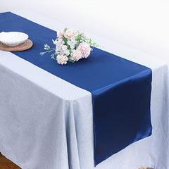 A smooth navy blue satin table runner draped over a light grey tablecloth with a floral centerpiece.