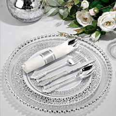 A silver plastic cutlery set with a napkin on a decorative charger plate.