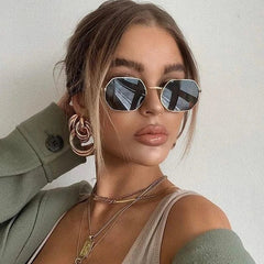 A woman wearing small, gold-framed hexagonal sunglasses with dark, reflective lenses.