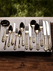 A set of gold-toned stainless steel flatware with ornate relief handles arranged on an open book.