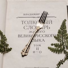 A vintage-style gold-toned metal fork with ornate relief detailing rests on an open book.