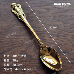 A gold-colored stainless steel spoon featuring an ornate vintage relief pattern on the handle.
