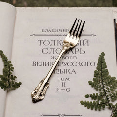 A gold-colored vintage-style fork with ornate relief detailing rests on an open book.