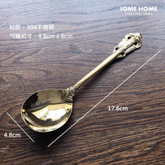 A gold-colored stainless steel spoon with an ornate relief handle design on a wooden surface.