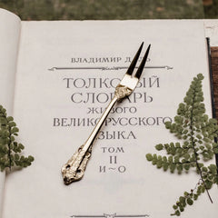 A gold-colored, ornate metal dessert fork with a relief pattern rests on an open book.