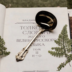 A gold-toned metal ladle with an ornate, embossed handle rests on an open book.