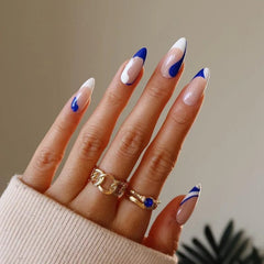 A hand displays long almond-shaped press-on nails with blue and white abstract French tip designs.