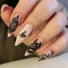 Long stiletto press-on nails featuring black snake and floral designs on a nude base.