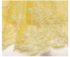 Close-up of yellow tulle fabric featuring intricate floral lace embroidery along the hem.