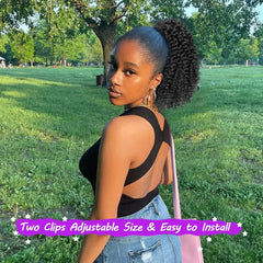 A woman wears a short, kinky curly afro ponytail extension in a park setting.