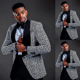 A man wears a black and white patterned jacquard blazer with a wide velvet lapel and black trousers.