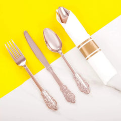 A set of rose gold plastic cutlery including a fork, knife, and spoon next to a wrapped napkin.