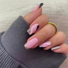 A hand displays square-shaped pink press-on nails with black, white, and glitter accents.