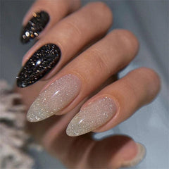 A hand displays almond-shaped nails with a mix of black glitter and shimmering nude polish.