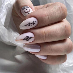 A hand displays almond-shaped pink press-on nails featuring delicate black line art designs.
