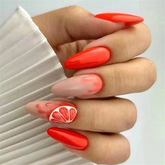 A hand displays almond-shaped press-on nails featuring a vibrant orange and citrus fruit design.