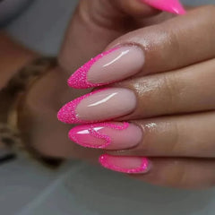 A hand displays almond-shaped press-on nails featuring a pink glitter French tip and swirl design.