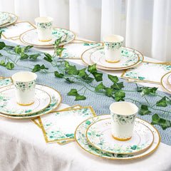 A set of disposable paper plates, cups, and napkins featuring a sage green leaf and gold rim design.