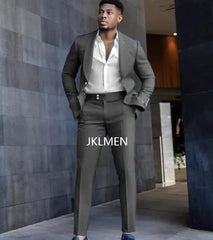 A man wears a slim-fit dark grey suit with a white button-down shirt and blue loafers.
