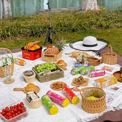 A white geometric patterned picnic blanket is spread on a lawn with food and baskets.