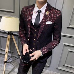 A man wears a slim-fit dark burgundy suit with a patterned texture, a white shirt, and a black tie.