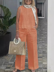 A woman wears a sleeveless orange cotton linen blouse and matching wide leg pants.