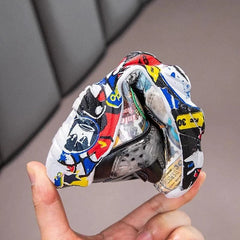 A hand holds a flexible children's sneaker featuring a colorful graffiti print pattern.