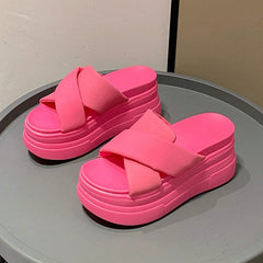 A pair of bright pink platform slide sandals with thick crisscross straps on a grey surface.