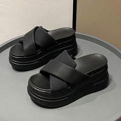 A pair of black platform slide sandals with thick crisscross straps on a chunky muffin sole.