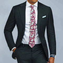 A man wears a slim fit black two-piece suit with a white shirt and a floral patterned tie.