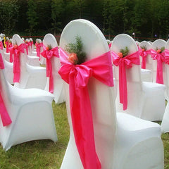 White spandex chair covers decorated with bright pink bows and small floral accents.