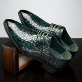A pair of dark green crocodile-patterned lace-up oxford shoes resting on a wooden block.