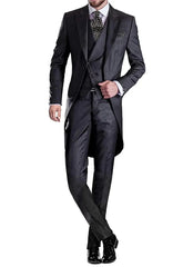 A man wearing a dark grey three-piece tailcoat suit with a polka dot tie and black dress shoes.