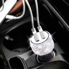 A dual USB car charger covered in sparkling rhinestones plugged into a vehicle console.
