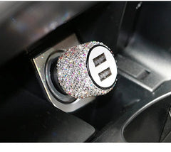 A dual USB car charger covered in sparkling rhinestones plugged into a vehicle power outlet.