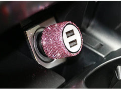 A pink rhinestone-encrusted dual USB car charger plugged into a vehicle power outlet.