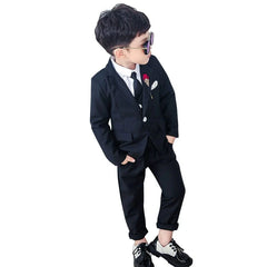 A young boy wears a black three-piece suit with a white shirt, black tie, and two-tone dress shoes.