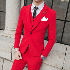 A man wears a slim-fit red three-piece suit with a white shirt, patterned tie, and rose lapel pin.