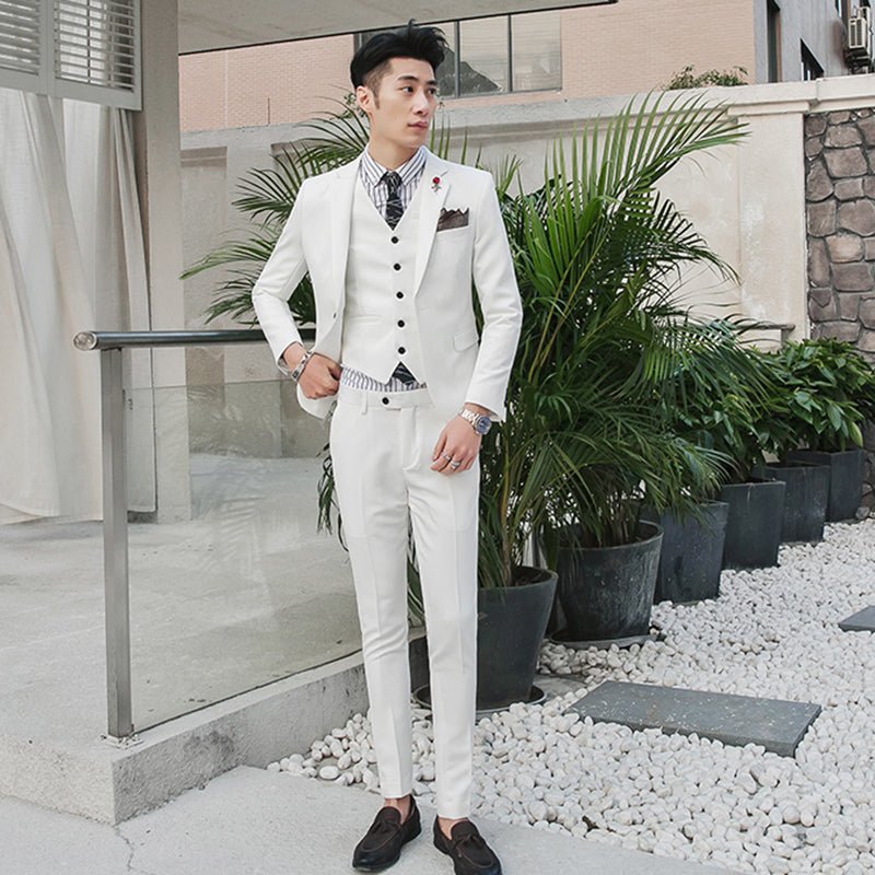 A man wears a slim-fit white three-piece suit with a striped shirt and dark loafers.