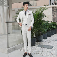 A man wears a slim-fit white three-piece suit with a striped shirt and dark loafers.