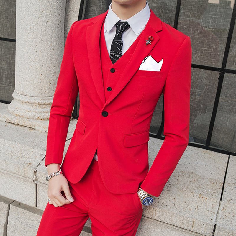A man wears a slim-fit red three-piece suit with a white shirt, patterned tie, and lapel pin.
