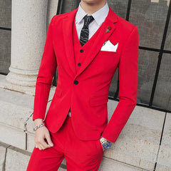 A man wears a slim-fit red three-piece suit with a white shirt, patterned tie, and lapel pin.