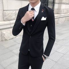 A man wears a slim-fit black three-piece suit with a white shirt, striped tie, and metal lapel pin.