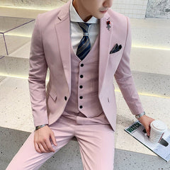 A man wears a slim-fit light pink three-piece suit with a patterned tie and a lapel pin.