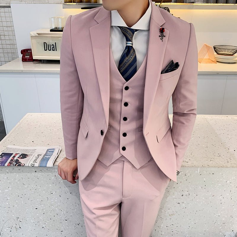 A man wears a slim-fit, light pink three-piece suit with a patterned tie and a lapel pin.
