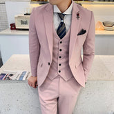 A man wears a slim-fit, light pink three-piece suit with a patterned tie and a lapel pin.